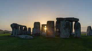 stone formations of stonehenge and the sun shining through part of the arrangement.