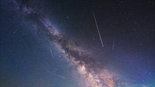 Milky way appears as a thick band of stars through the sky, which is also filled with some meteor streaks.