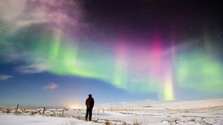 Man looking at colorful auroras in north Iceland. Snow covered ground with stars and Northern lights dancing in the sky.