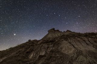 a starry sky with the big dipper above and Arcturus shining bright on the left of the sky with large rock formations below.