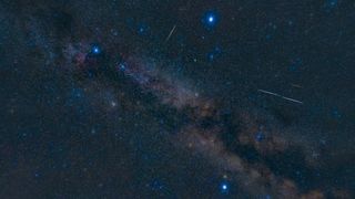 three distinct bright blue stars make up the summer triangle, there are some long white streaks of light from meteors.