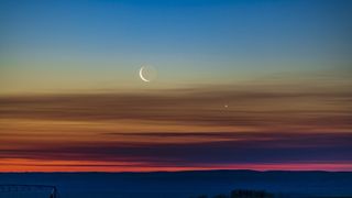 The conjunction of the waning crescent moon with Venus as they were rising low in the northeast dawn sky in southern Alberta, Canada. Earthshine is visible on the dark side of the moon. The sky exhibits the wonderful transition of colours from the orange at the horizon through the spectrum to the blues at top