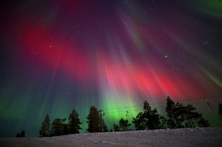 northern lights in sky appear as red and green ribbons and pillars of light